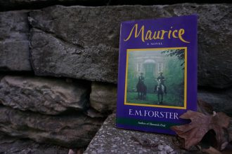 "Maurice" by E.M. Forester leans against a stone wall with fallen leaves off to the side.